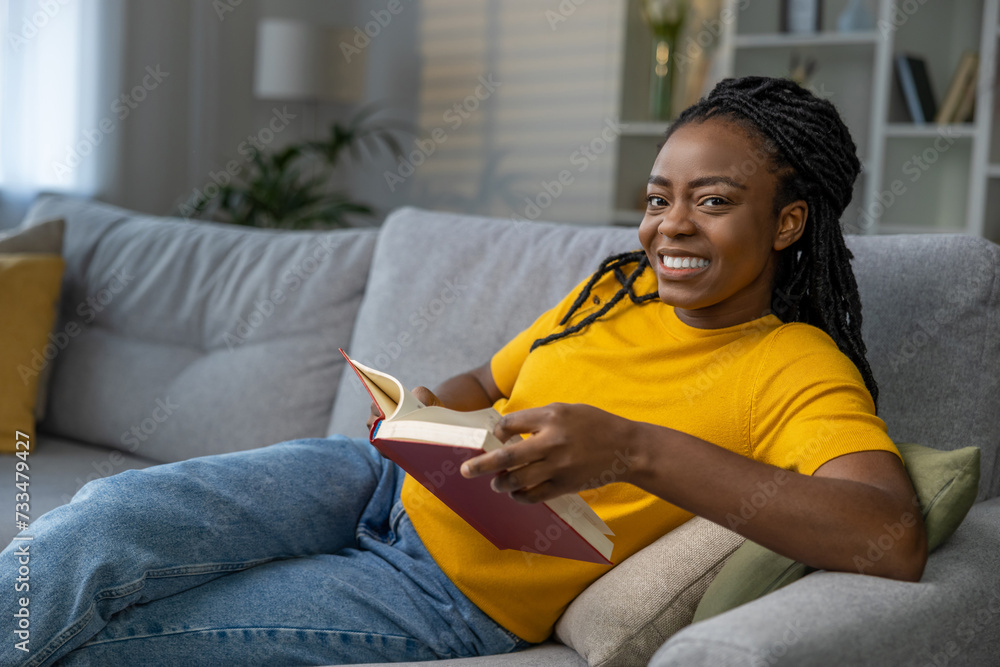 Dark-skinned cute young woman reading a book and smiling