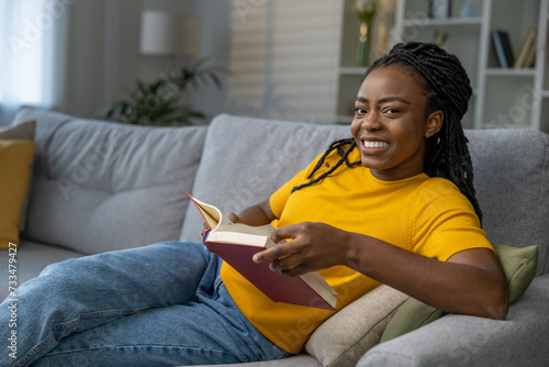 Dark-skinned cute young woman reading a book and smiling