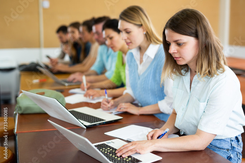 Photos Group of young students searches for information on a laptop and writes it down in a copybooks, studying in a university