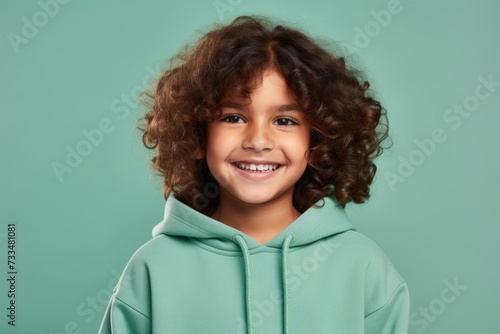 Little curly girl in a green hoodie on a turquoise background