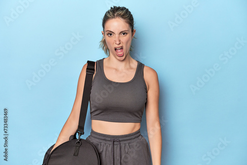Blonde athlete with gym backpack screaming very angry and aggressive.