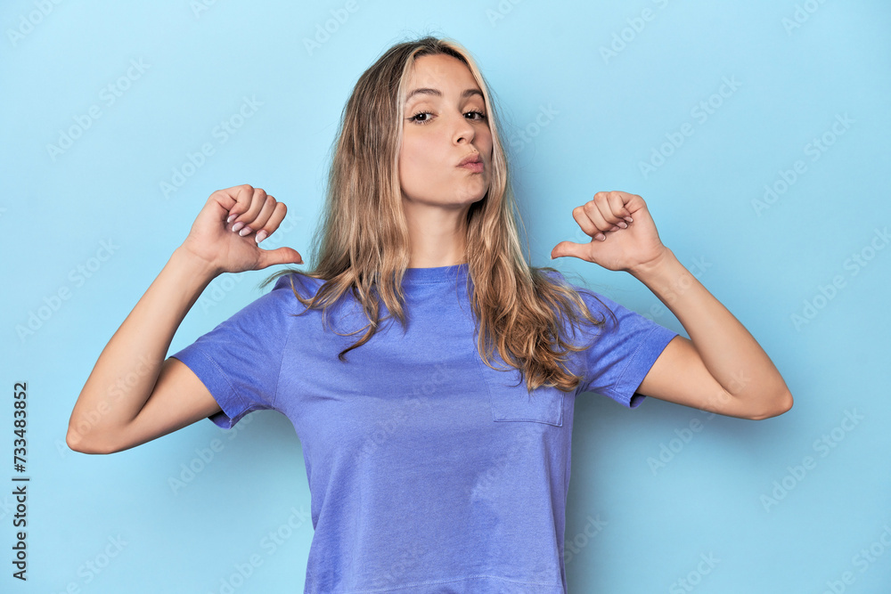 Fototapeta premium Blonde young caucasian woman in blue studio feels proud and self confident, example to follow.