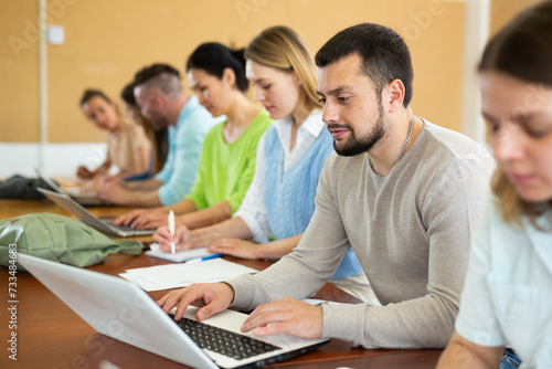 Group of students studying in the auditorium at study time, searches for information on a laptop and writes it out in a ..copybooks