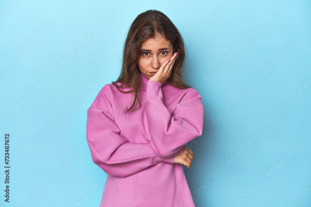 Teen girl in cozy pink sweatshirt on blue who is bored, fatigued and need a relax day. Teen girl in cozy pink sweatshirt on blue who is bored, fatigued and need a relax day.