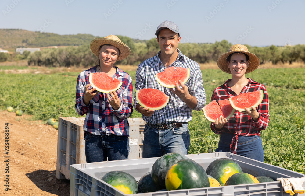 Group photo of positive farmers holding juicy sclices of watermelon and smiling.