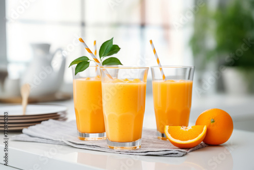 Orange smoothie in tall glasses in white modern kitchen on the table
