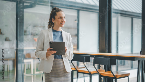 Business analytics concept, Confident female professional smiling and holding a digital tablet in a contemporary office space with natural light.