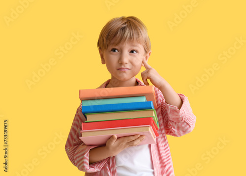 thoughtful little boy with stack of books against yellow wall