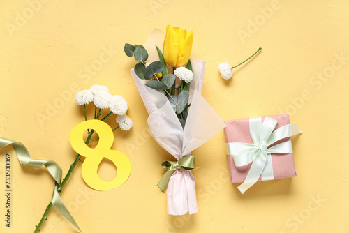 Fototapeta Naklejka Na Ścianę i Meble -  Mini bouquet of beautiful spring flowers in wrapping paper with figure 8 and gift box on yellow background. International Women's Day