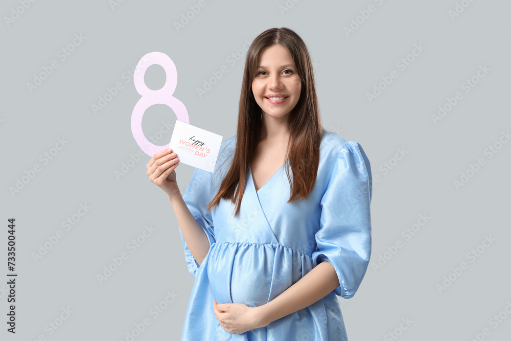 Beautiful young pregnant woman with figure 8 made of paper and greeting card on grey background. International Women's Day Beautiful young pregnant woman with figure 8 made of paper and greeting card on grey background. International Women's Day