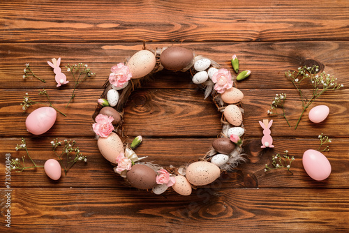 Stylish Easter wreath decorated with eggs and flowers on wooden background. Top view