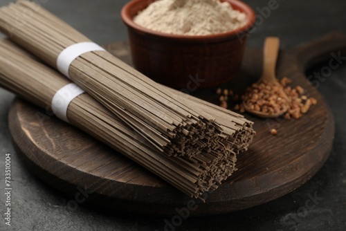 Uncooked buckwheat noodles (soba), flour and grains on black table, closeup photo
