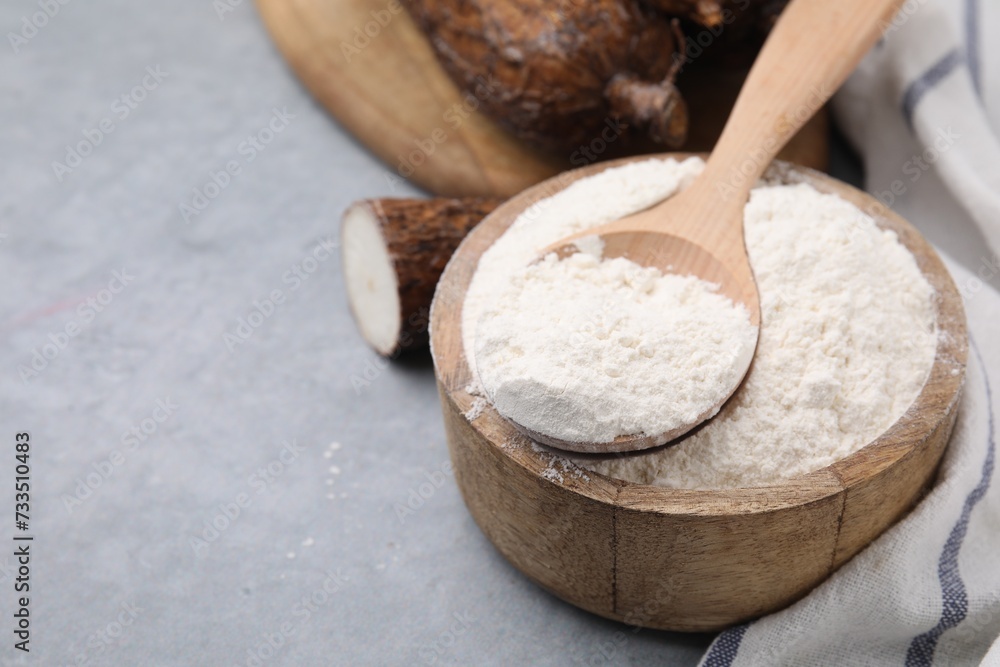 Wooden bowl and spoon with cassava flour on grey table, closeup. Space for text Wooden bowl and spoon with cassava flour on grey table, closeup. Space for text