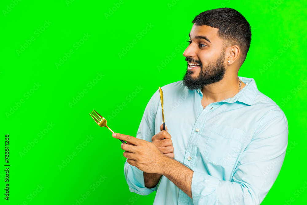 Ready to eat. Hungry Indian man waiting for serving dinner dishes with with restlessness holding cutlery fork knife, will appreciate delicious restaurant meal. Guy isolated on chroma key background