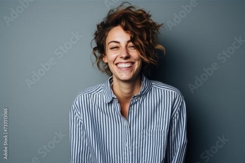Portrait of a happy young woman laughing against a grey background.