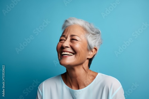 Portrait of happy senior asian woman laughing against blue background.