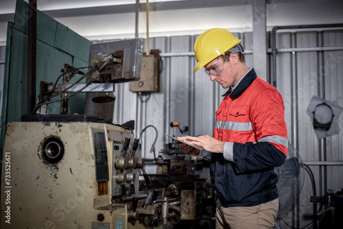 Industry engineer wearing safety uniform control operating lathe grinding machine working with detail tablet computer on hand in industry factory  is metal manufacture industry concept.