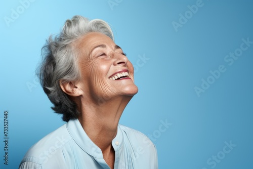 Portrait of a happy senior woman laughing against blue background with copy space