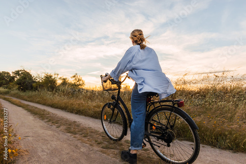 back view of a blonde woman on a bike in a field during sunset