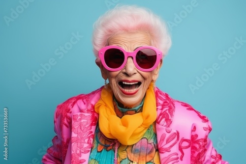 Portrait of a happy senior woman with pink sunglasses on blue background © Iigo