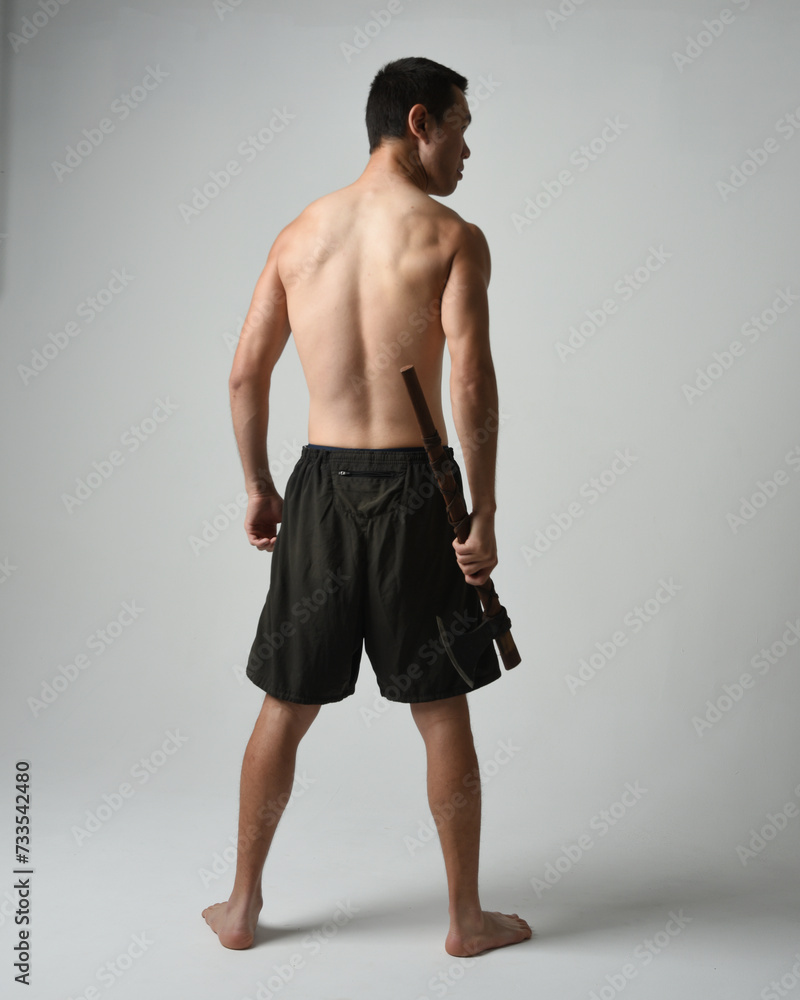Full length portrait of fit handsome shirtless asian male model, Holding viking axe weapon, standing in warrior training action pose, isolated on white studio background. Full length portrait of fit handsome shirtless asian male model, Holding viking axe weapon, standing in warrior training action pose, isolated on white studio background.