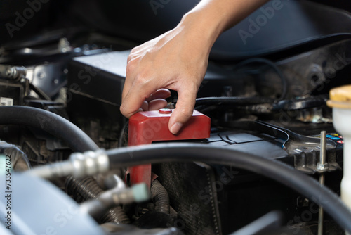 A woman inspecting the battery of a car, standing in front of the car with the hood open, and she is looking at the battery.