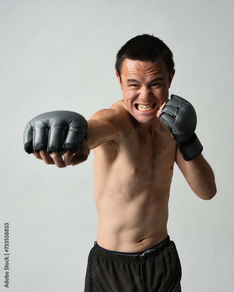 Close up portrait of fit asian male model, shirtless with muscles. Wearing gym shorthand boxing gloves, gestural punching pose. Isolated on a white studio background. Close up portrait of fit asian male model, shirtless with muscles. Wearing gym shorthand boxing gloves, gestural punching pose. Isolated on a white studio background.