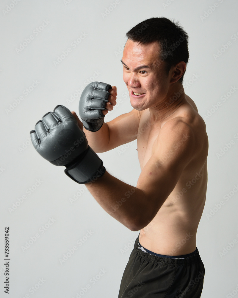 Close up portrait of fit asian male model, shirtless with muscles. Wearing gym shorthand boxing gloves, gestural punching pose. Isolated on a white studio background. Close up portrait of fit asian male model, shirtless with muscles. Wearing gym shorthand boxing gloves, gestural punching pose. Isolated on a white studio background.