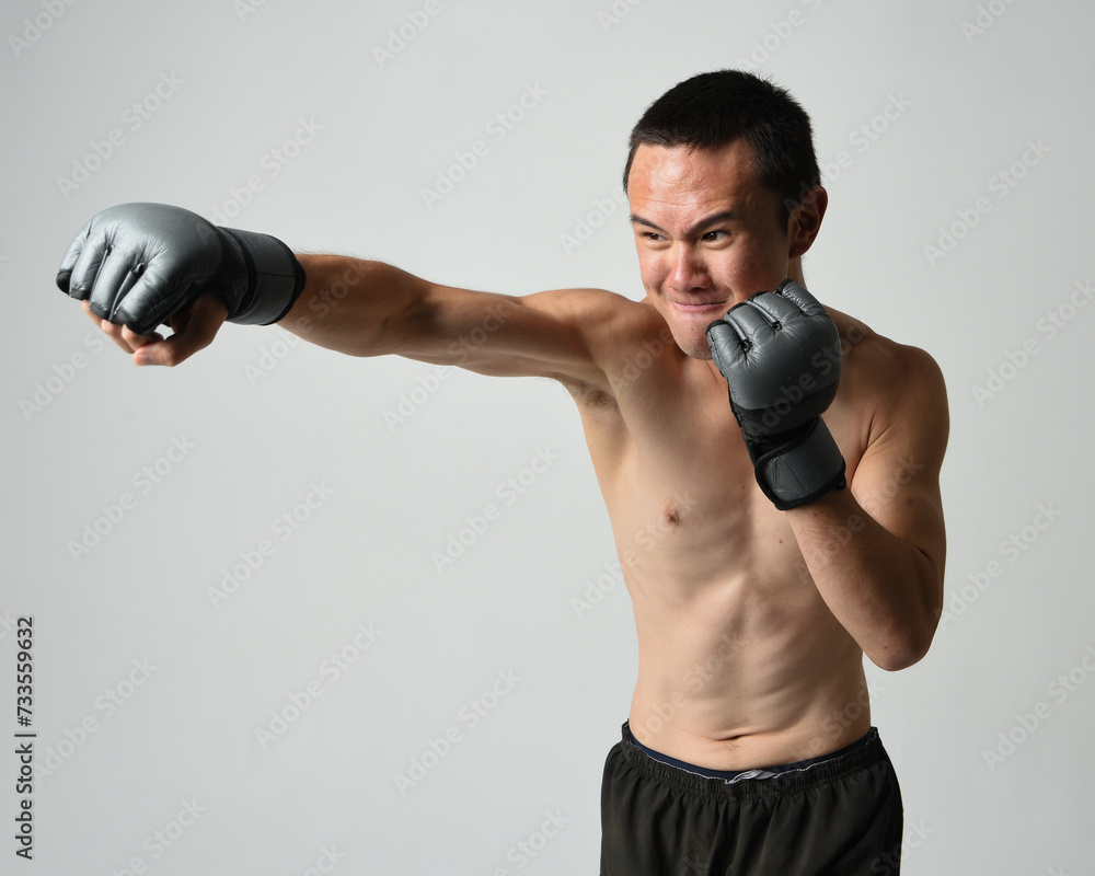 Close up portrait of fit asian male model, shirtless with muscles. Wearing gym shorthand boxing gloves, gestural punching pose. Isolated on a white studio background. Close up portrait of fit asian male model, shirtless with muscles. Wearing gym shorthand boxing gloves, gestural punching pose. Isolated on a white studio background.