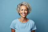 Cheerful mature woman looking at camera and smiling while standing against blue background