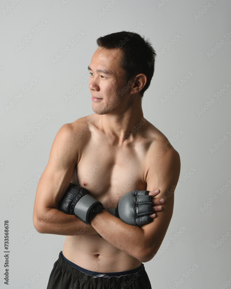 Close up portrait of fit asian male model, shirtless with muscles. Wearing gym shorthand boxing gloves, gestural punching pose. Isolated on a white studio background. Close up portrait of fit asian male model, shirtless with muscles. Wearing gym shorthand boxing gloves, gestural punching pose. Isolated on a white studio background.