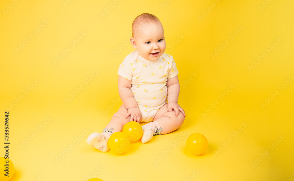Happy baby girl with yellow balls on yellow background. Joyful infant looking away, smiling. Happy baby girl with yellow balls on yellow background. Joyful infant looking away, smiling.