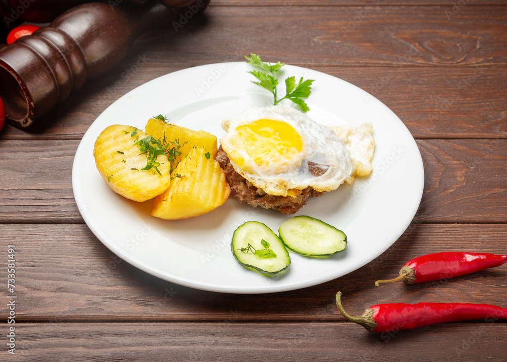Beefsteak with egg and boiled potatoes. On a wooden background.