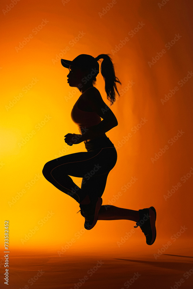 Silhouette of woman jogger in activewear jumping
at studio against a vivid orange background, fitness lifestyle Silhouette of woman jogger in activewear jumping
at studio against a vivid orange background, fitness lifestyle