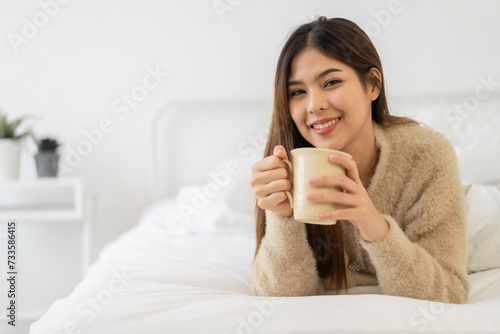 Portrait of smiling happy cheerful beauty pretty asian woman relaxing drinking and looking at cup of hot coffee or tea.Girl felling enjoy having breakfast in holiday morning vacation on bed at home