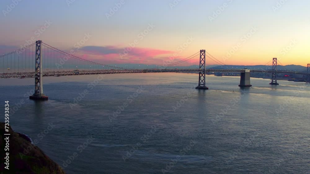 Aerial Lockdown Shot Of Illuminated Oakland Bay Bridge Over Rippled Sea Against Dramatic Clouds At Sunset - San Francisco, California Aerial Lockdown Shot Of Illuminated Oakland Bay Bridge Over Rippled Sea Against Dramatic Clouds At Sunset - San Francisco, California