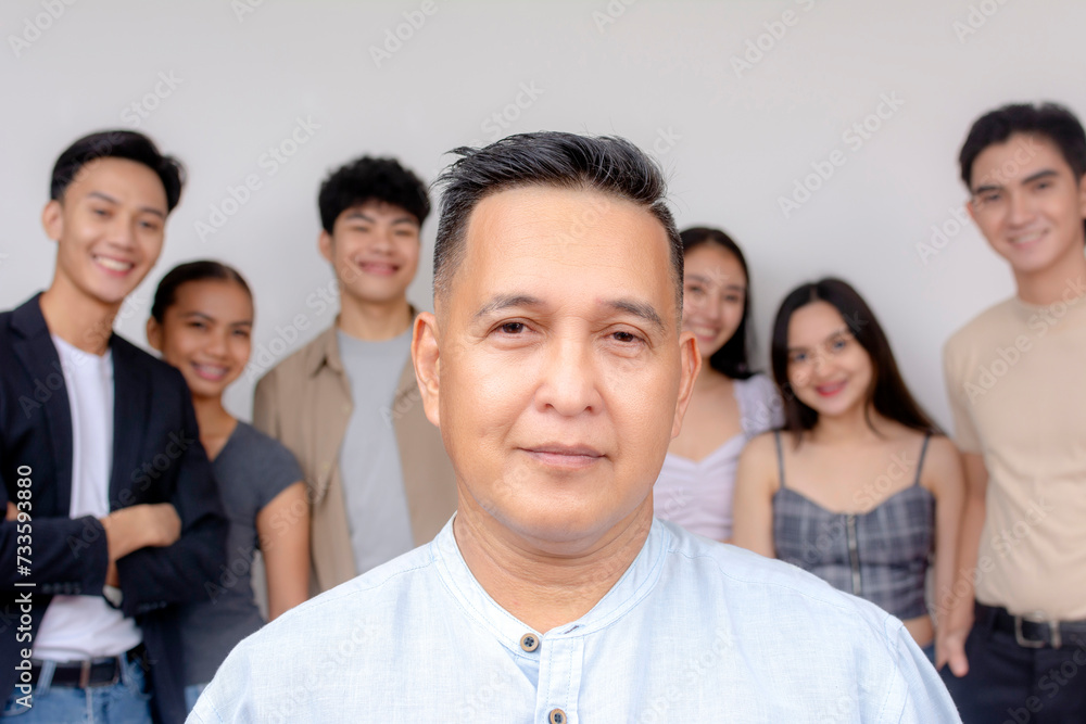 A middle aged man posing in front of his proteges or employees. A founder of a startup company with a youthful workforce. A middle aged man posing in front of his proteges or employees. A founder of a startup company with a youthful workforce.