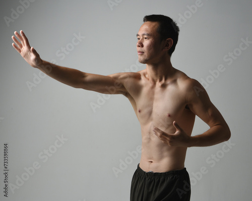 Close up portrait of fit asian male model, shirtless with muscles. gestural ti chi inspired posing with arms reaching out. Isolated on a white studio background with moody silhouette.