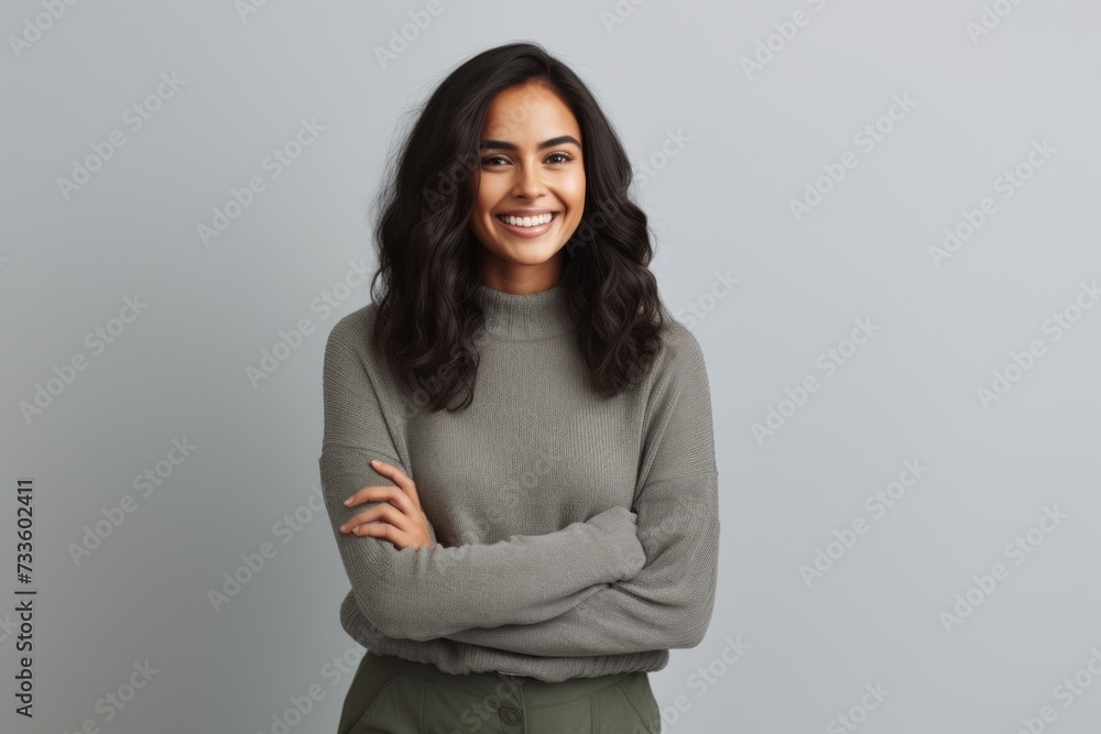 Portrait of a happy young woman standing with arms crossed against grey background Portrait of a happy young woman standing with arms crossed against grey background