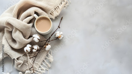 Top view of a cozy beige cashmere scarf on a light gray background with a cup of coffee and a cotton sprig Autumn winter concept photo
