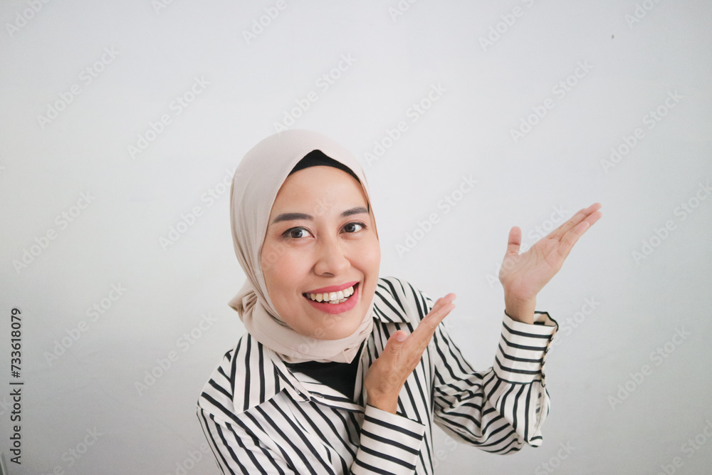 Happy Asian Muslim woman wearing a head scarf and stripped blouse pointing at the copy space on the side of her, isolated by a white background Happy Asian Muslim woman wearing a head scarf and stripped blouse pointing at the copy space on the side of her, isolated by a white background