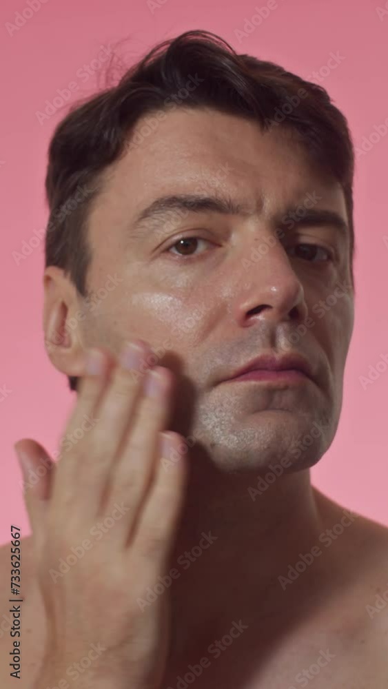 Vertical shot of male mid-adult applying cream on face isolated in pink background Vertical shot of male mid-adult applying cream on face isolated in pink background