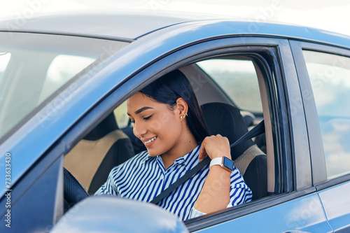 Smiling woman putting on the seatbelt before start driving the car
