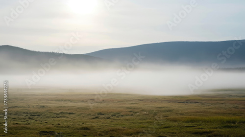 Foggy landscape in a field against the backdrop of mountains and hills in the early morning. © Evgeniia