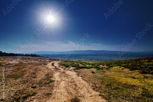 A summer landscape with a dirt road in rural mountainous terrain and the sun in the frame.