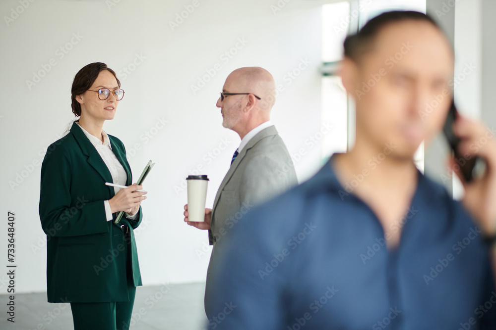 Focus on young female manager with documents standing in front of mature male boss with cup of coffee during conversation at meeting Focus on young female manager with documents standing in front of mature male boss with cup of coffee during conversation at meeting