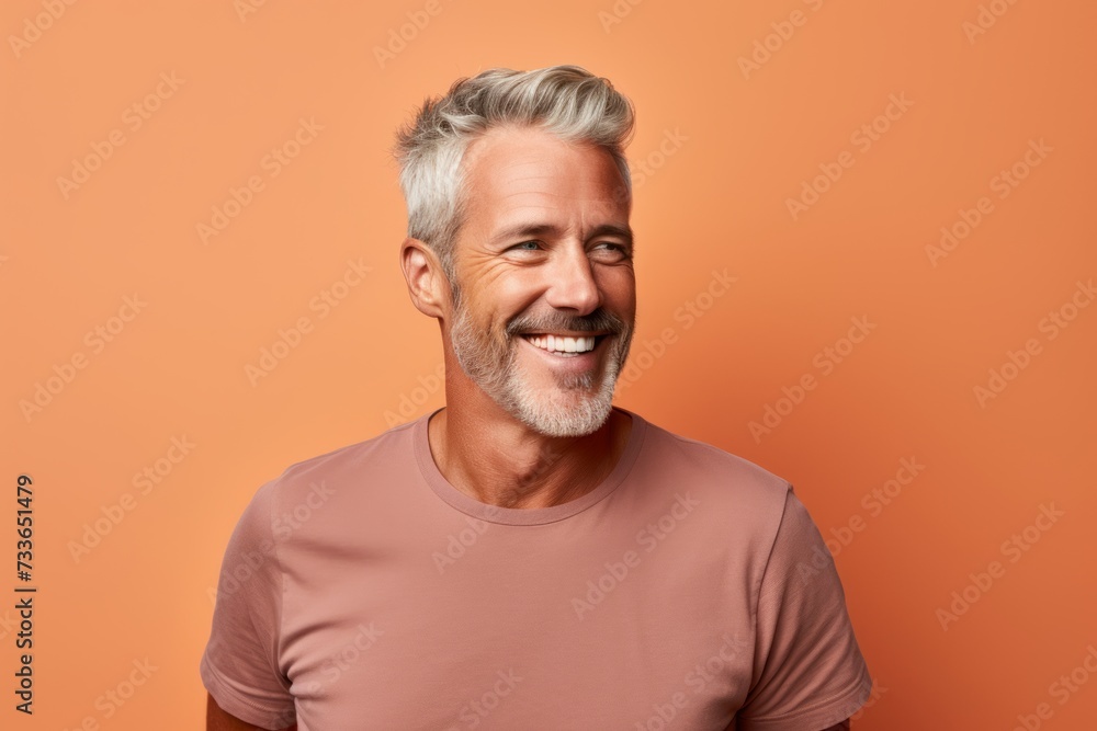 Cheerful mature man with grey hair and beard is looking at camera and smiling while standing against orange background Cheerful mature man with grey hair and beard is looking at camera and smiling while standing against orange background