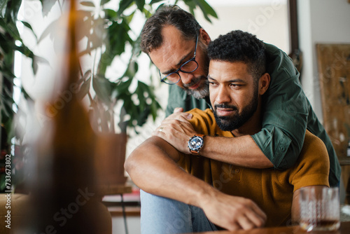 Man hugging best friend, supporting each other, drinking whiskey and talking. Discussing problems and drowning sorrows in alcohol. Concept of male friendship, bromance.