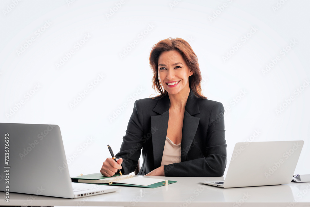 Studio shot of an attractive mid aged woman sitting at desk and using laptop against isolated white background Studio shot of an attractive mid aged woman sitting at desk and using laptop against isolated white background