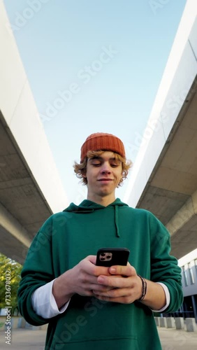 Handsome student looking mobile phone and walking at city closeup